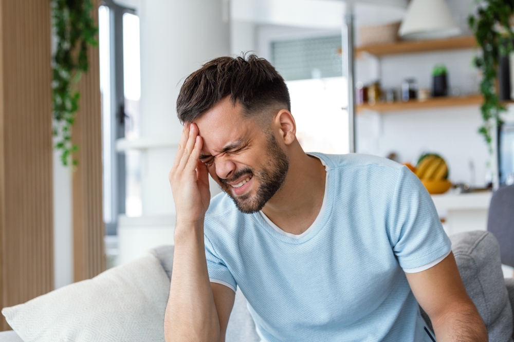 young man suffering from headache at home, touching his temples, copy space