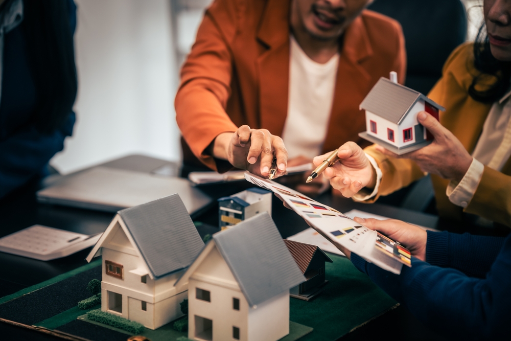 Asian real estate team engaged in a discussion, with two men and a woman focusing on a house model on a table